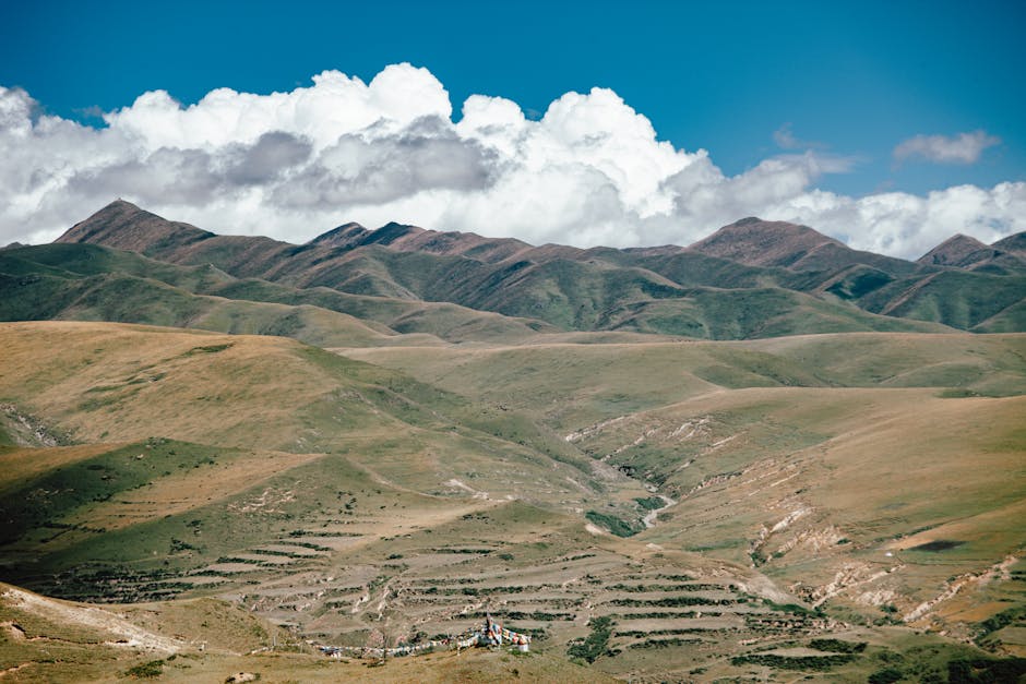 Scenic view of rolling mountains and lush valleys under a clear blue sky with fluffy clouds.